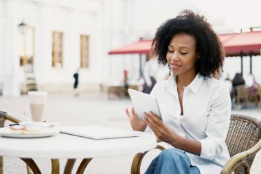 Müşteriye e-posta ile bir mesaj yazar. Sokaktaki öğrenci tablet üzerinde çalışıyor. Blogcu kıvırcık saçlı, Afro-Amerikan görünümlü genç kadın şehirdeki bir iş merkezinin yakınında..