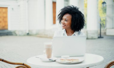 Müdür bir yazlık kafede dizüstü bilgisayarla çalışıyor. Afro görünümlü bir kız öğrenci bilgisayara bir mesaj yazar. Çok güzel gülümsüyor, beyaz gömlek rahat, kıvırcık saçlı..