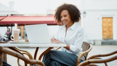 Afro görünümlü müdür bir yazlık kafede bilgisayar başında çalışıyor. Öğrenci çevrimiçi çalışıyor. Bir iletiyi e- posta ile müşterilere yazdırır.