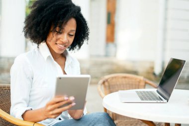 Bir öğrenci aboneliklerine bir sosyal ağ üzerinden dizüstü bilgisayara mesaj basıyor. Afro-Amerikan görünümlü bir kadın bilgisayarda çalışıyor. Kıvırcık saçlı ve beyaz gömlekli..