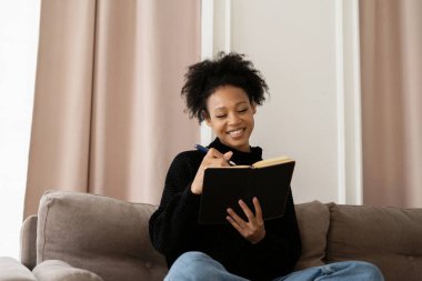 Serbest çalışan bir kadın günlük tutar, evdeki kanepede oturur..