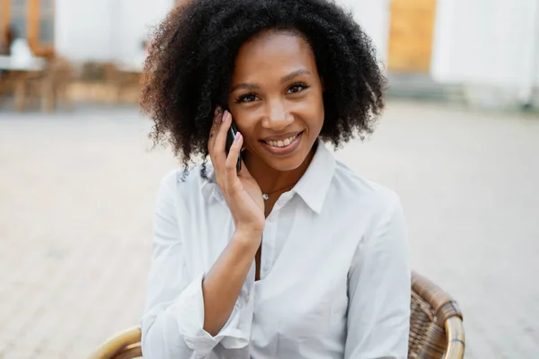 一个女人对着一个与朋友通电话的非洲裔学生笑了 自由职业者用的是小工具 — 图库照片