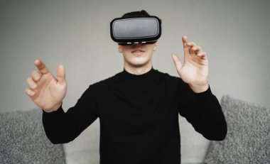 Evde sanal gerçeklik oynuyor. Kanepede VR ile oturuyor.