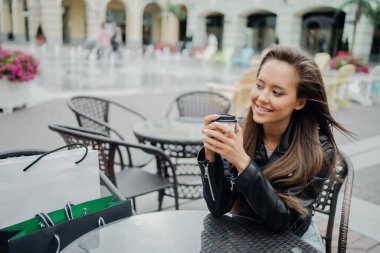 Elinde sıcak kokulu bir kapuçino tutuyor, gülümsüyor. 