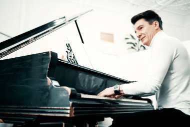 Evde piyano çalıyor. Güzel klasik müzik çalıyor. Akustiği güzel. Bir müzik enstrümanı üzerine notalarla çalışan çalışmalar. Yetişkin erkek, 50-60 yaşlarında, müzik okulunda öğretmen..