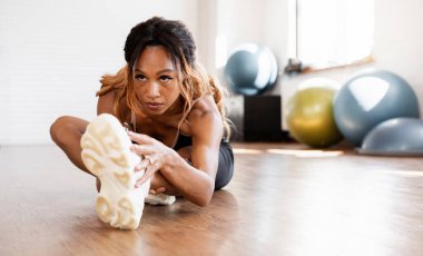 Güç antrenmanından önce vücudu germek. Sportif ve sağlıklı bir yaşam tarzı. Güçlü bir Amerikalı kadın spor salonunda antrenman yapıyor. Spor için farklı ekipmanlarla kardiyo egzersizleri için fitness stüdyosu.