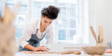 Profesyonel bir zanaatkar seramiklerden yemek yapar. Dekoratif ürün stüdyosunda üniformalı bir çalışan. Bir kadın çömlek atölyesinde çalışıyor..