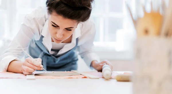 用瓷器做一个盘子 一个穿围裙的女人在一家陶器作坊工作 一个专业的工匠用陶瓷做盘子 装饰产品工作室里穿制服的员工 — 图库照片