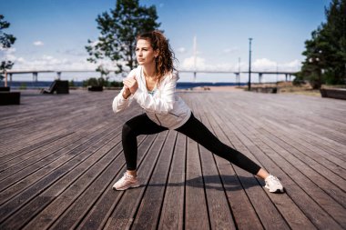 Şehirde spor haberleri. Profesyonel bir antrenör antrenmandan önce ısınma egzersizleri yapar. Sporcunun sağlıklı bir yaşam tarzı var. Kilo vermek için kardiyo eğitimi. Kadınlar için rahat kıyafetler..