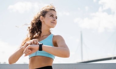 Sportif bir esmer fitness antrenörü akıllı bir saate bakar ve kalori ve kardiyoyu kontrol eder. İnce vücutlu ve rahat giysiler. Sağlıklı yaşam tarzı kavramı.