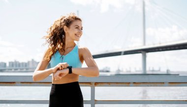 Ellerdeki nabzı ölçmek için akıllı bir saat kullanıyor. Sokakta spor yapan bir kadın. Fitness ve sağlıklı bir yaşam tarzı. Antrenör vücudu germek için egzersiz yapar..