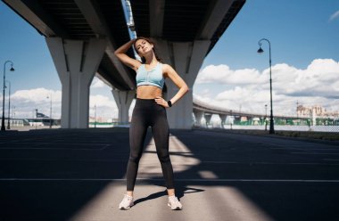 Formda kalmak için kaslarını esnetme egzersizleri aktiftir. Şehrin sokaklarında antrenman yapan bir kadın figürü. Güçlü, kendinden emin bir atlet, koşucu sağlıklı bir hayat sürüyor..