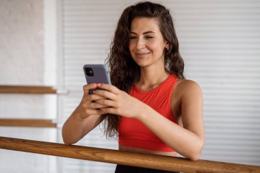Telefon fitness uygulamasını kullanıyor. Bir aerobik koçu egzersiz yapar. Sportif bir kadın ve sağlıklı bir yaşam tarzı. Antrenman için rahat dar giysiler. İnce şekilli kardiyo dersleri.