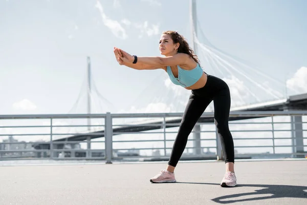 Koç caddede egzersiz yapıyor. Sağlıklı bir yaşam tarzı. Bir kadın esneme egzersizi yapar. Spor giyim sektöründe bir sporcu. Şehirde açık hava fitness.