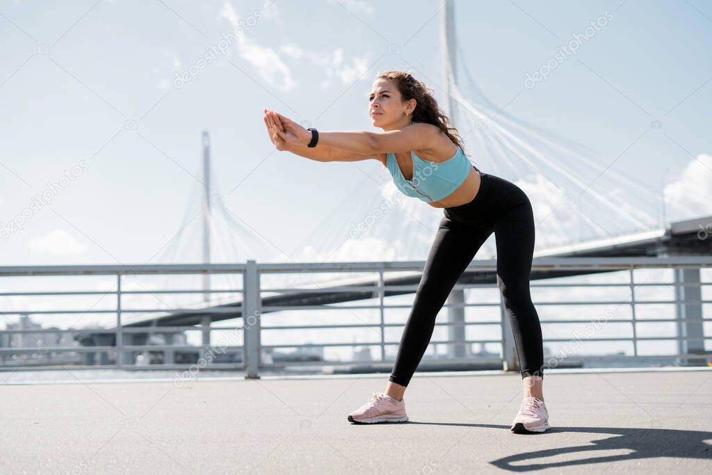 Coach exercises on the street. Healthy lifestyle. A woman does a stretching workout. An athlete in sportswear. Outdoor fitness in the city.