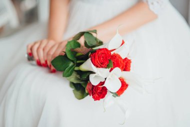 Gelinin elleri, zengin kırmızı ve beyaz düğün buketini tutuyor.