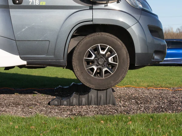 The front wheel of a motorhome recreational vehicle has been raised up by driving vehicle up a black levelling block.Level.RV.