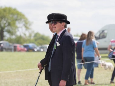Badminton-Gloucestershire-İngiltere-11 Mayıs 2022 - Badminton At Mahkemeleri 'nde takım elbiseli ve melon şapkalı iki erkek kahya onları arka planda gün ışığında yürüyerek geçti