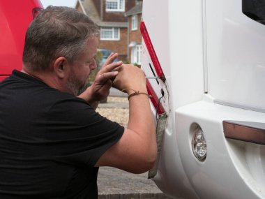 Bir elektrikçi, bir karavan eğlence aracının arka fren lambası kapaklarını kaldırmak ve onarmak için tornavida kullanır..