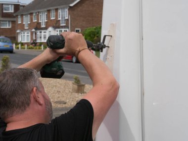 Bir tamirci, bir karavan eğlence aracının fiber cam kaplamasında delik açmak için kablosuz bir matkap üzerinde ayarlanabilir bir delik açma aracı kullanır.
