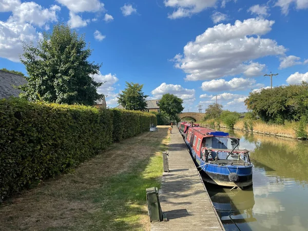 Traditional narrowboats are moored on a rural canal with towpath beside them.Sunny blue sky and white clouds day.Pontoon
