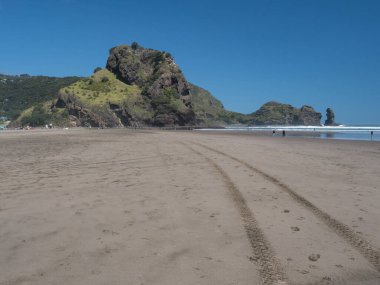 Piha Sahili 'nin kuzeyindeki Yeni Zelanda adasında araç izleri Te Piha.Volkanik kaya oluşumu olarak bilinen Aslan kayasına çıkıyor. Uzaktan görülebilen bir kaya yığını..