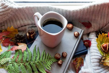 Penceredeki gri fincanda sonbahar kahvesi. Çarşaflar ve kitaplarla dağılmış.