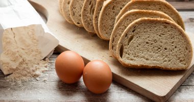 Dilimlenmiş taze ekmek ve kırsal bir masada bir bıçak. Yakınlarda un ve yumurta var.