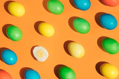 Paskalya yumurtalarının parlak turuncu bir arka planı ve soyulmuş bir yumurtası var. Paskalya 'nın bahar kompozisyonu. Minimum düzlük.