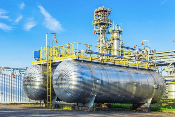 İki metal kap bir gaz işleme tesisinin arka planında ve mavi bir gökyüzünde duruyor..