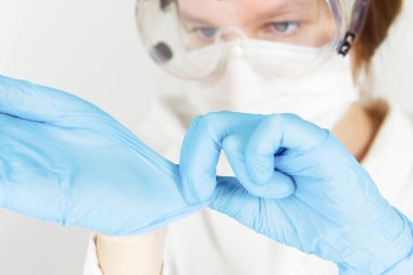 Maske takan ve gözlük takan bir doktor ameliyattan sonra tıbbi eldiven çıkartıyor..
