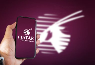 Doha, Katar, Temmuz 2021: Ekranda Katar Havayolları uygulaması olan bir el telefonu tutuyor ve Arap antilobu koyu kiraz rengi arka planda bulanıklaşıyor.