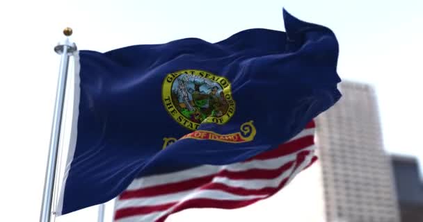 アイダホ州の旗がアメリカの星やストライプの旗を背景に風になびかせています 1890年7月3日 アイダホ州は合衆国に加盟した第43番目の州となった — ストック動画