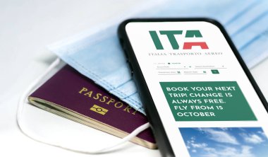 Roma, İtalya, Ekim 2021: ameliyat maskesi ve pasaport için ekrandaki ITA uygulaması ile telefon görüşmesi. ITA, 15 Ekim 2021 'den itibaren yeni İtalyan bayrak taşıyıcısı. Pandemik zamanlarda seyahat