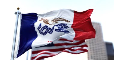 ABD 'nin Iowa eyaletinin bayrağı rüzgarda dalgalanırken arka planda Amerikan yıldızları ve çizgili bayrağı belirsizleşti. Üç dikey çizgi. Ortadaki şeritte elinde kurdele olan bir kartal var..