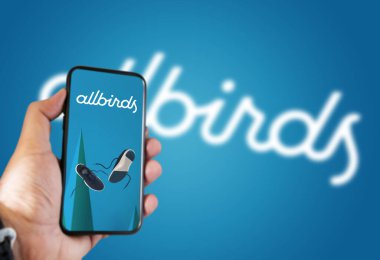 San Francisco, ABD, Ekim 2021: ekranda Allbirds mobil uygulaması olan bir telefonu tutan logo mavi arka planda bulanıklaştı. Tüm kuşlar ayakkabı ve giysi tasarlar ve satar.