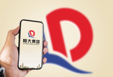 Guangzhou, Çin, Ekim 2021: ekranda Evergrande logosu olan bir telefonu tutan ve arka planda logosu bulanık olan. Evergrande, Çin 'in en büyük ikinci emlak geliştiricisidir.