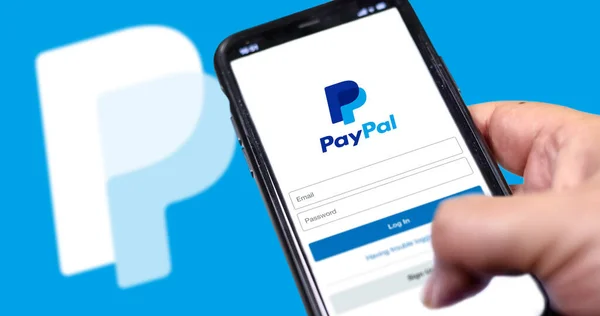 ローマ イタリア 2021年2月16日 画面上のPaypalアプリのログインページと背景にぼやけたPaypalのロゴとスマートフォンを保持手 ショッピング オンラインアプリケーション — ストック写真