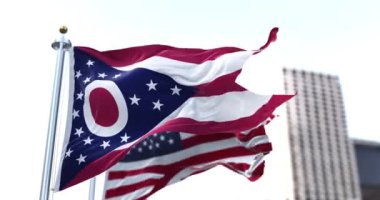 the flag of the US state of Ohio waving in the wind with the American flag blurred in the background. Ohio state flag is the only non-rectangular flag of all the U.S. states