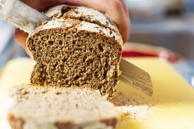 Slicing fresh rye bread with a big knife in a a domestic kitchen. Healthy food and source of fiber. Bakery product