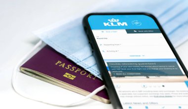Amsterdam, NED, Temmuz 2021: koruyucu maske ve pasaportun üzerinde yatan ekrandaki KLM havayolları uygulaması ile telefon. Coronavirus salgını sırasında seyahat güvenliği ve kısıtlamaları