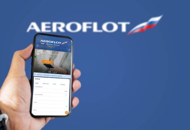 Moskova, Ocak 2022: Aeroflot Rus Hava Yolları uçuş rezervasyon uygulaması ile el ele tutuşmak. Aeroflot logosu mavi arka planda bulanıklaştı. Uçak biletlerini ayırtıyorum.