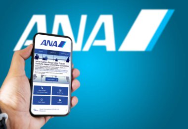 Tokyo, JAP, Ocak 2022: ANA All Nippon Airways uçuş rezervasyon uygulaması ile el ele tutuşmak. Ana logo mavi arka planda bulanıklaştı. Uçak biletlerini ayırtıyorum.