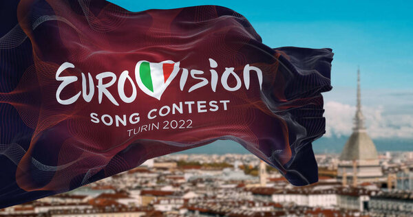 Турин, Италия, январь 2022: Флаг конкурса песни "Евровидение-2022" размахивает на ветру логотипом с размытым ландшафтом Турина. 2022 год пройдет в Италии с 10 по 14 мая
