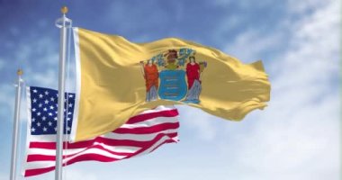 New Jersey eyalet bayrağı, Amerika Birleşik Devletleri bayrağıyla birlikte dalgalanıyor. Arka planda açık bir gökyüzü var. New Jersey, ABD 'nin kuzeydoğu bölgelerinde bir eyalettir.