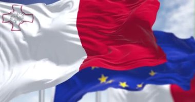 Detail of the national flag of Malta waving in the wind with blurred european union flag in the background on a clear day. Democracy and politics. European country. Selective focus.