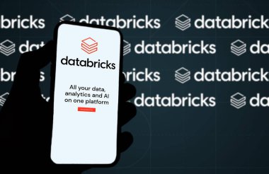 San Francisco, CA, US, May 2022: hand holding a phone with Databricks company web page on screen. In background the logo Databricks blurred and repeated. Databricks is an enterprise software company clipart