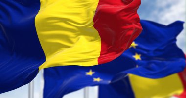 Detail of the national flag of Romania waving in the wind with blurred european union flag in the background on a clear day. Democracy and politics. European country. Selective focus.