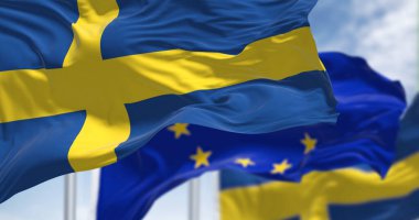 Detail of the national flag of Sweden waving in the wind with blurred european union flag in the background on a clear day. Democracy and politics. European country. Selective focus.