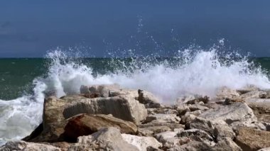 Dalgalar köpük ve su damlacıklarıyla kayaların üzerinde kırılıyor. Doğanın enerjisi. Çevre ve dalga